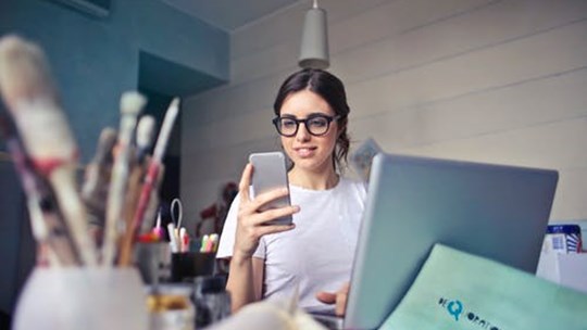 Kvinde sidder med computer og smartphone
